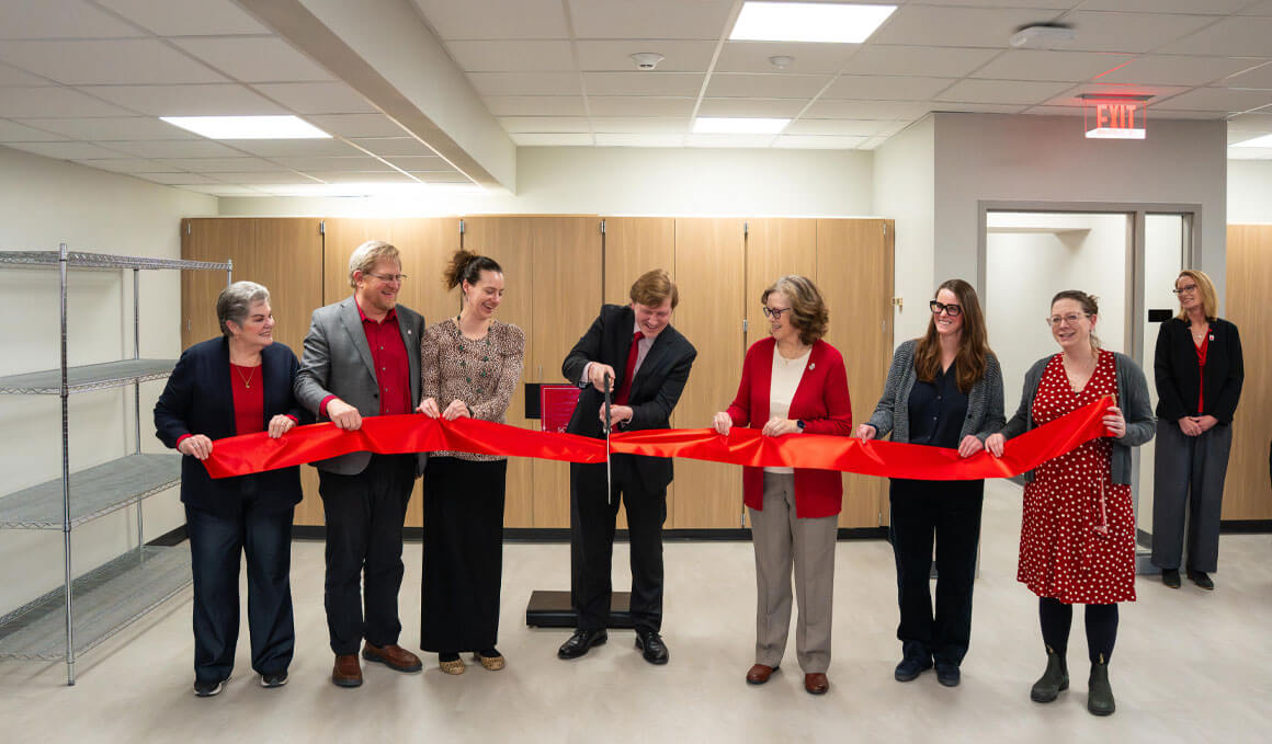 Anthony Krus stands in the middle of a group and holds a giant pair of scissors, getting ready to cut the bright red ribbon during the ribbon-cutting ceremony at the new ARCHLAB.