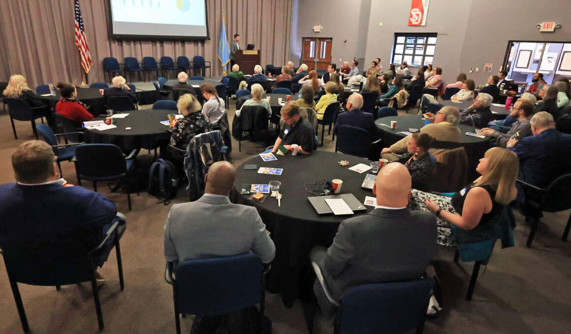 A photo from USD's 2025 Chiesman Center for Democracy conference, where a group of people are sitting in a conference room, listening to a speaker.