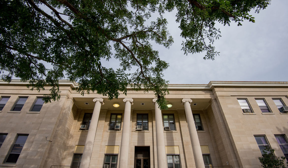 A close up image of the exterior of the College of Arts and Sciences building, with tree leaves cutting into view in the top left corner of the image.