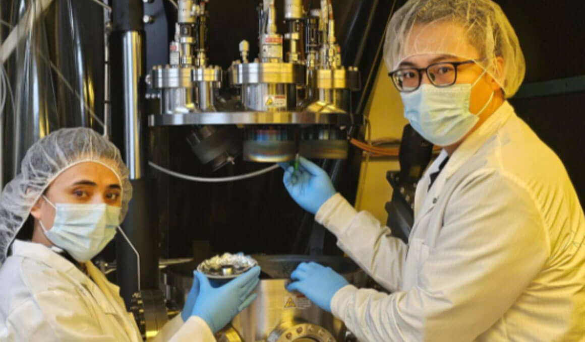 Dongming Mei, Ph.D., and his student researcher stand in a laboratory while standing next to a microscope and holding up petri dishes.