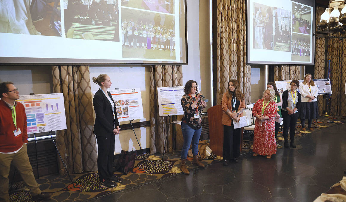 Several people stand at the front of a room presenting at the Arts Leadership Institute. Behind them are posters and projected slides, suggesting research presentations, project showcases or conference-style talks related to the arts.