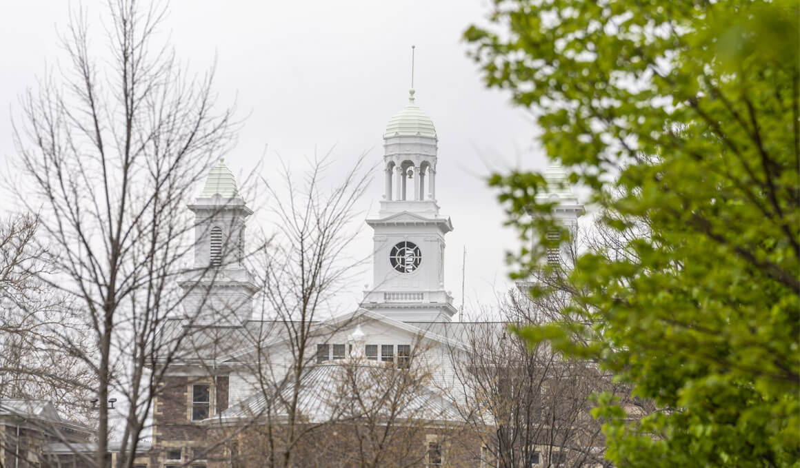 A close-up of Old Main on the USD campus, with bare and green trees in the foreground.