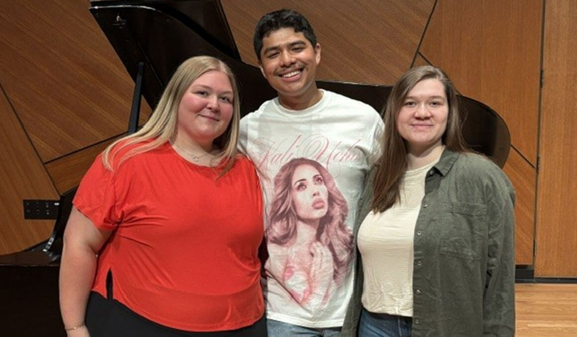 Three out of the four USD students, who have advanced to the semifinal round of the National Student Auditions, stand on a stage in front of a grand piano.