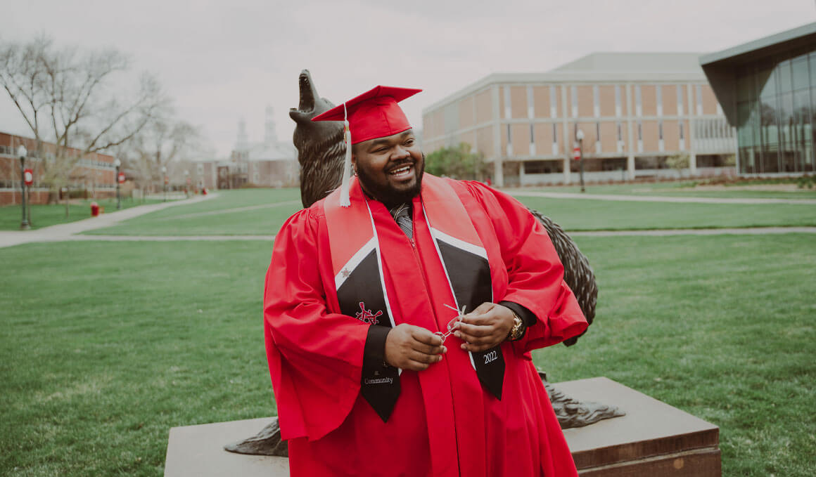 Marcus Destin stands in his graduation regalia in front of the Coyote Legacy statue on the USD campus in Vermillion.
