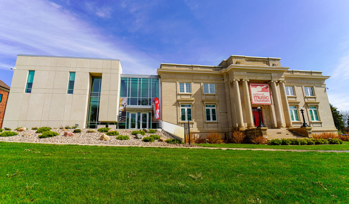 The National Music Museum sits on the University of South Dakota's campus on a sunny summer day, with a green law outstretched in the front of it.
