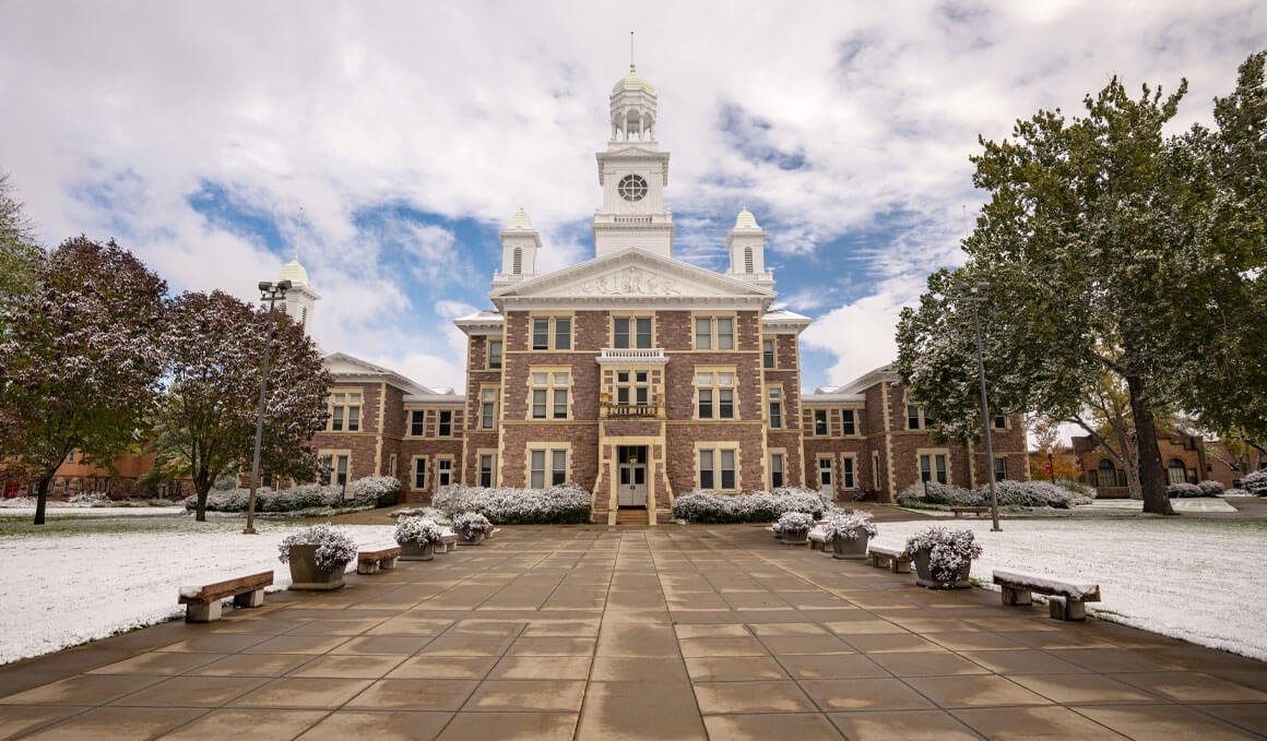 Old Main sits on a sunny USD campus, with light snow in the foreground.
