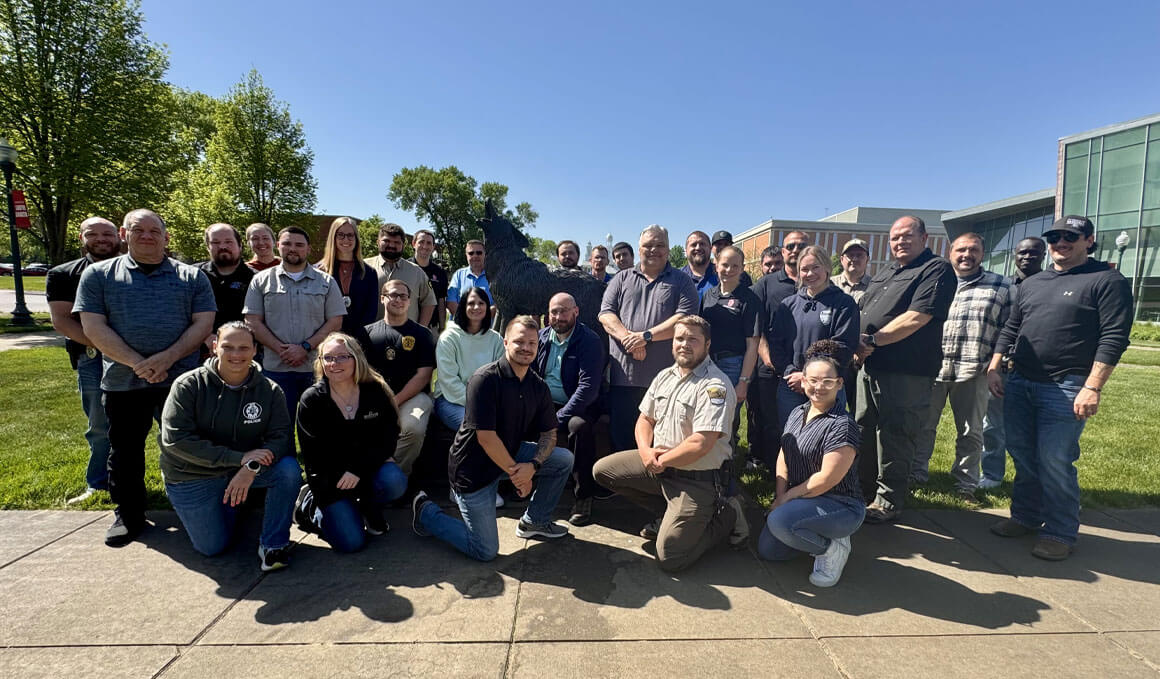 A group of UPD Training attendees pose for a photo on the USD campus, outdoors on a sunny day. 