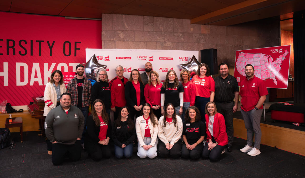 The USD Alumni and Foundation team stand in front of USD branded banners, a map and balloons at the 2025 Unite for USD event.