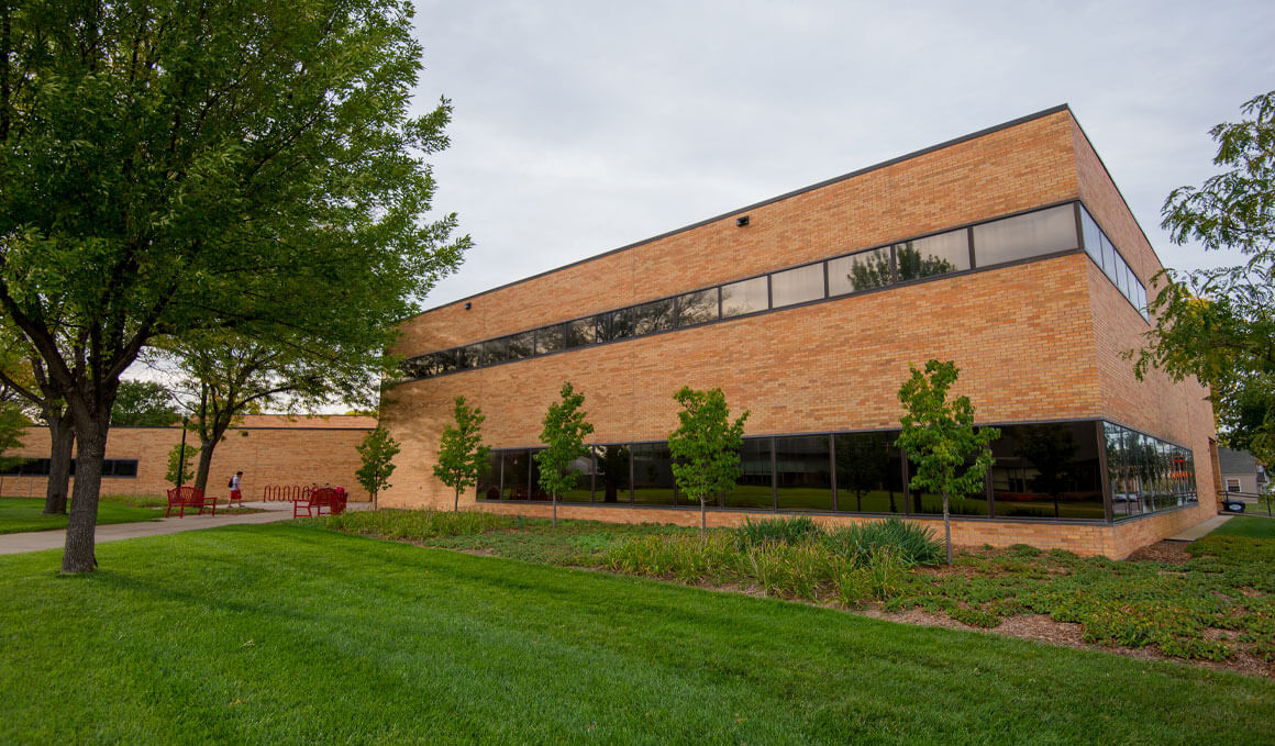 This photo shows the exterior of the Knudson School of Law building. It sits on the USD campus on a sunny day, with green grass, plants and trees in its forefront.