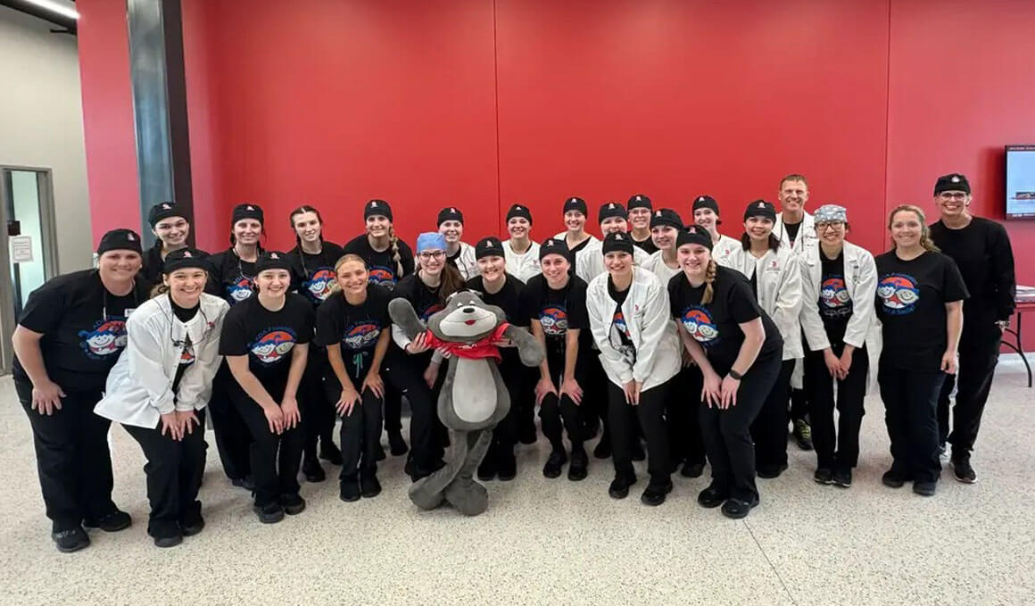 USD Dental Hygiene students pose for a photo in front of a red wall at the "Give Kids a Smile" event.