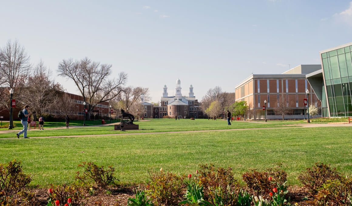 A photo of the USD campus, with Old Main in the background and green grass and students, as well as the Coyote Legacy statue, in the foreground.