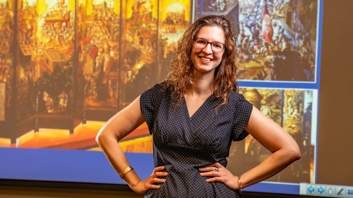 Sara Lampert poses in front of a screen with historical graphics on it. 