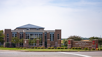 A street view of the USD – Sioux Falls campus that shows a building and a sign that says University of South Dakota Sioux Falls.