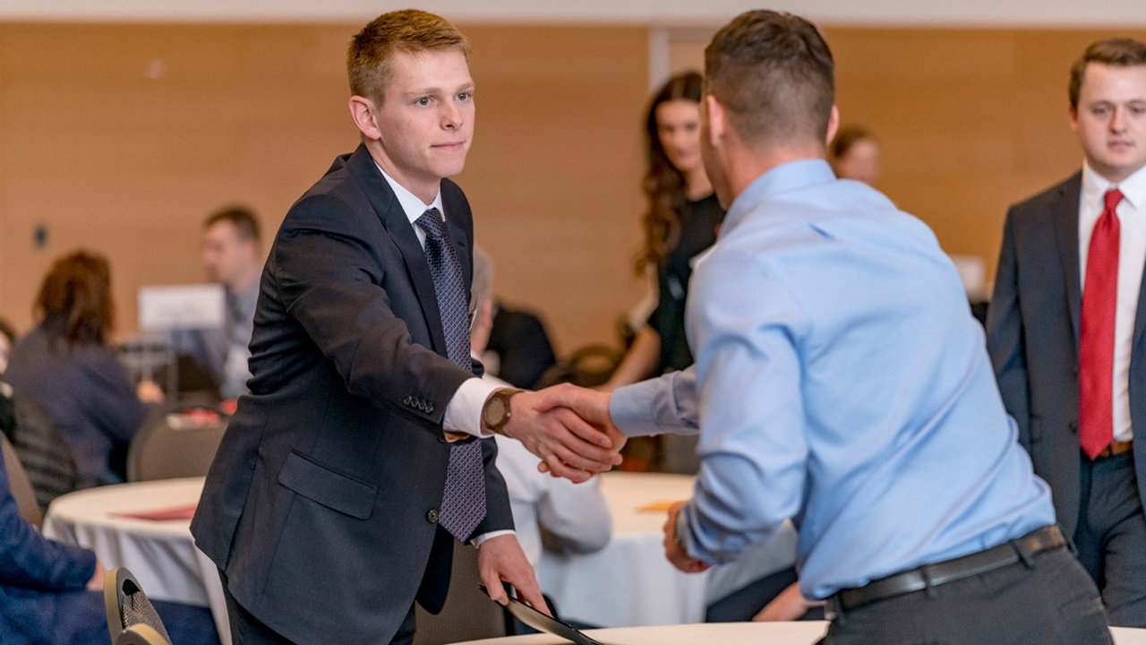 Two business students shake hands over a table.