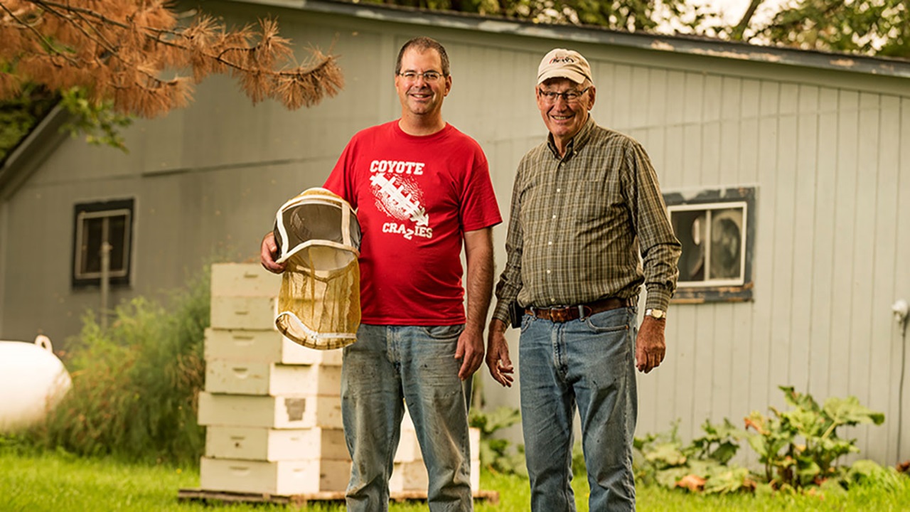 Dan Van Peursem and his uncle standing near their bees, holding their equipment Dan Van Peursem and his uncle standing near their bees, holding their equipment