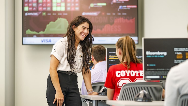 A USD student stands over another, looking onto a computer screen with Bloomberg technology. They are in the Ellis Lab.