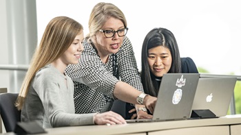 Emily Quinn helps two students looking onto a laptop.