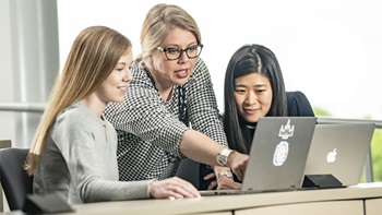 Emily Quinn helps two students looking onto a laptop. Emily Quinn helps two students looking onto a laptop.