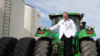 A man in a white USD lab coat stands in front of a green tractor.