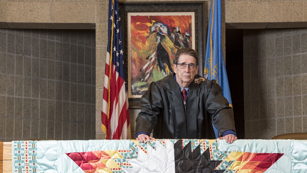 Frank Pommersheim standing in the Knudson School of Law courtroom. He has a straight face while looking at the camera. He is wearing his robes. Frank Pommersheim standing in the Knudson School of Law courtroom. He has a straight face while looking at the camera. He is wearing his robes.