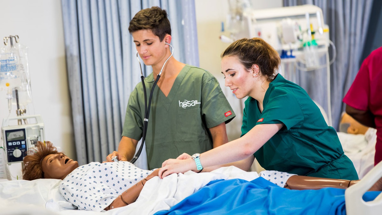 Two students check the pulse and heartbeat of a simulation manikin. Two students check the pulse and heartbeat of a simulation manikin.