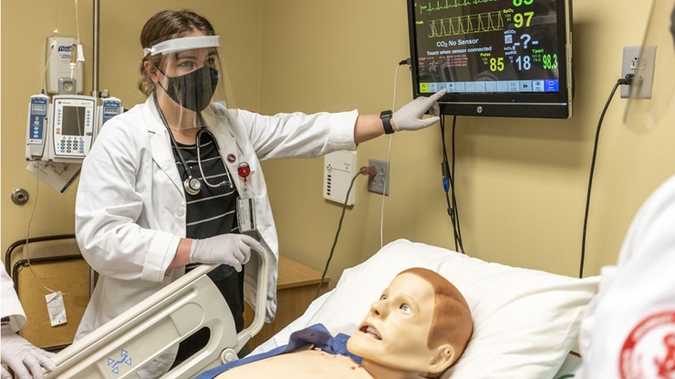 A USD student stands over a manikin, reading its chart and explaining something to their team. A USD student stands over a manikin, reading its chart and explaining something to their team.
