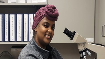 Iman Omar in the lab, sitting near a microscope.
