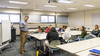 Kevin Reins teaches in front of a classroom, showing a group of students a project.