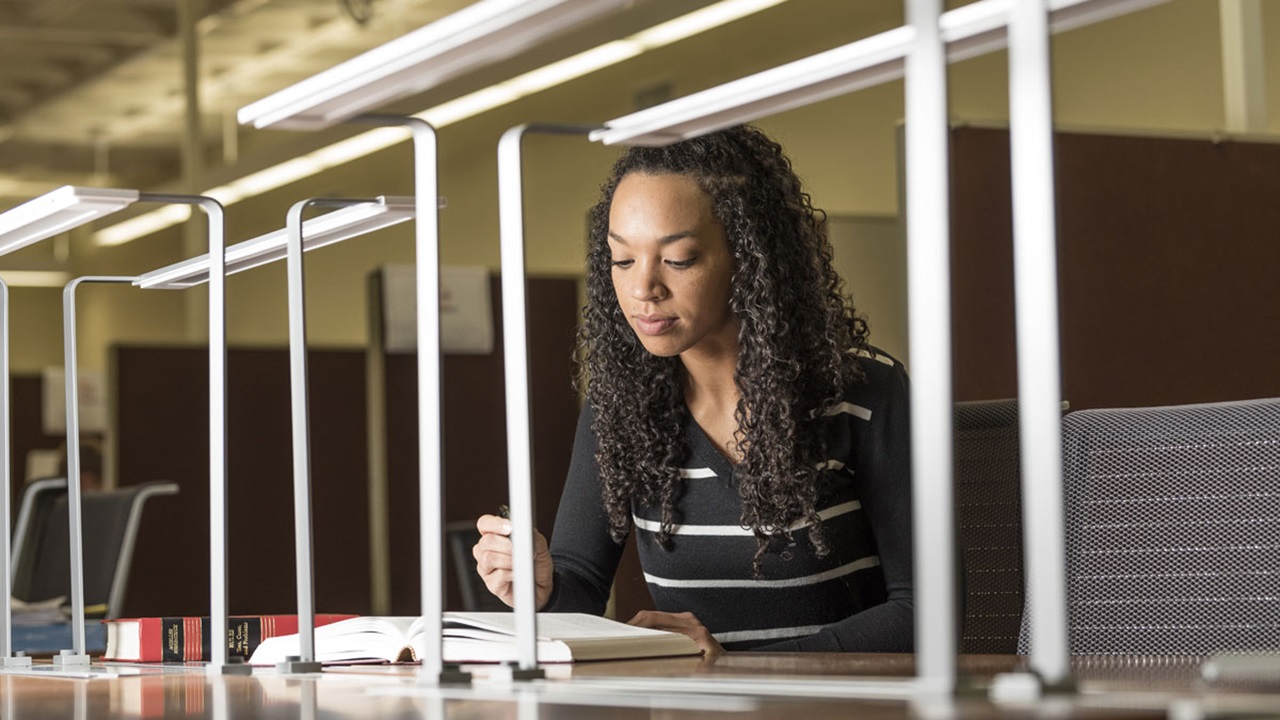 A Knudson School of Law student studying. They are looking down at the textbook on the desk. A Knudson School of Law student studying. They are looking down at the textbook on the desk.