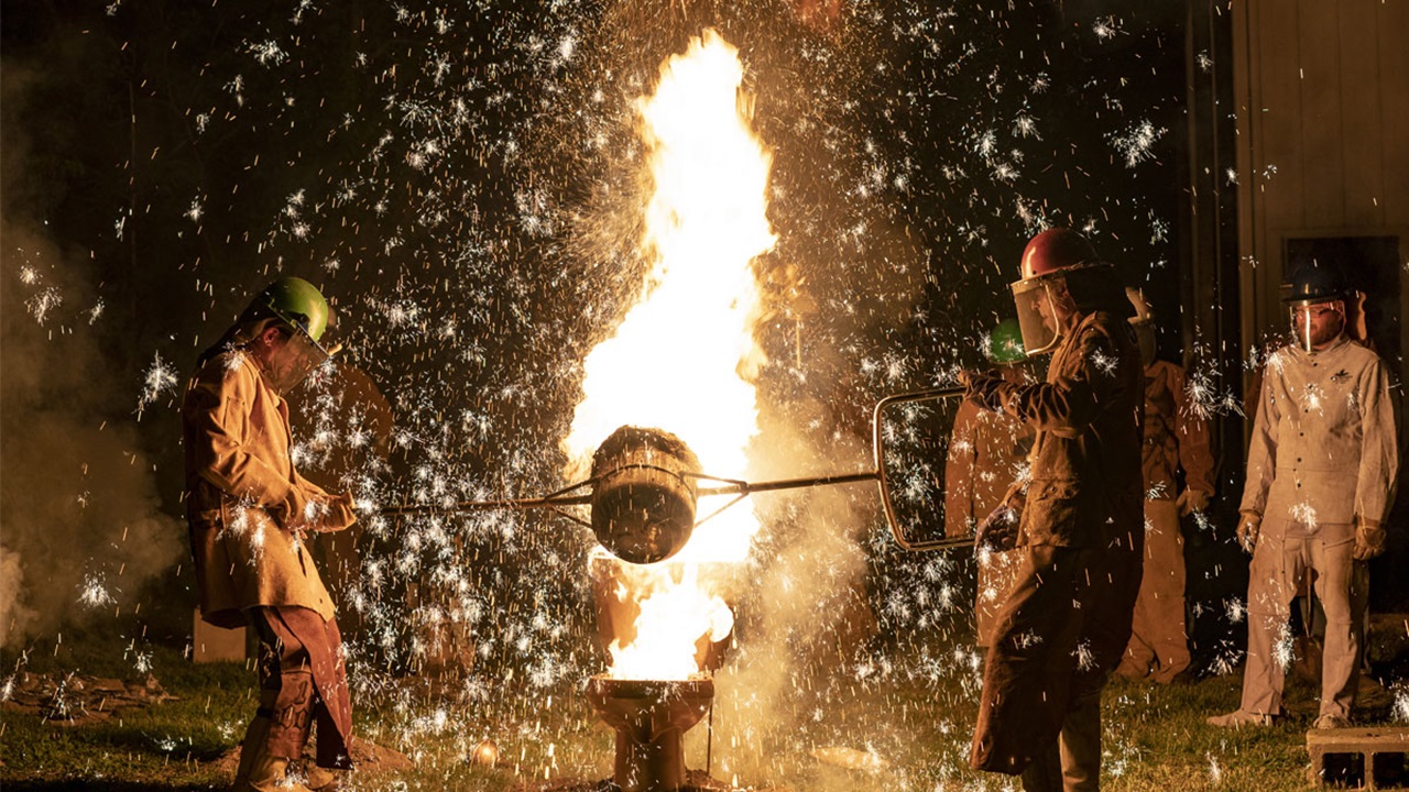 Two people pour hot iron into a mold. Sparks fly. Two people pour hot iron into a mold. Sparks fly.