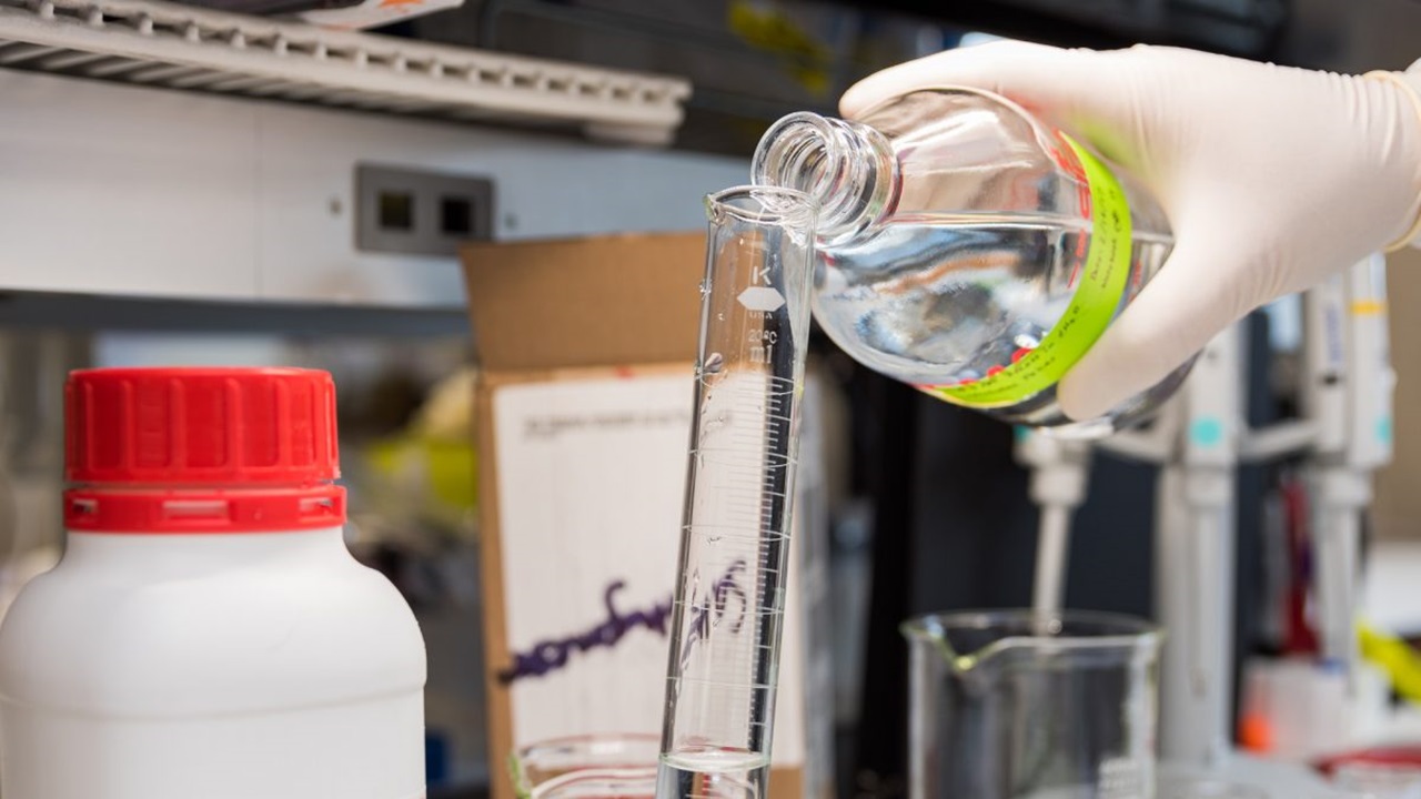 A hand pours liquid into a test tube to make hand sanitizer.
