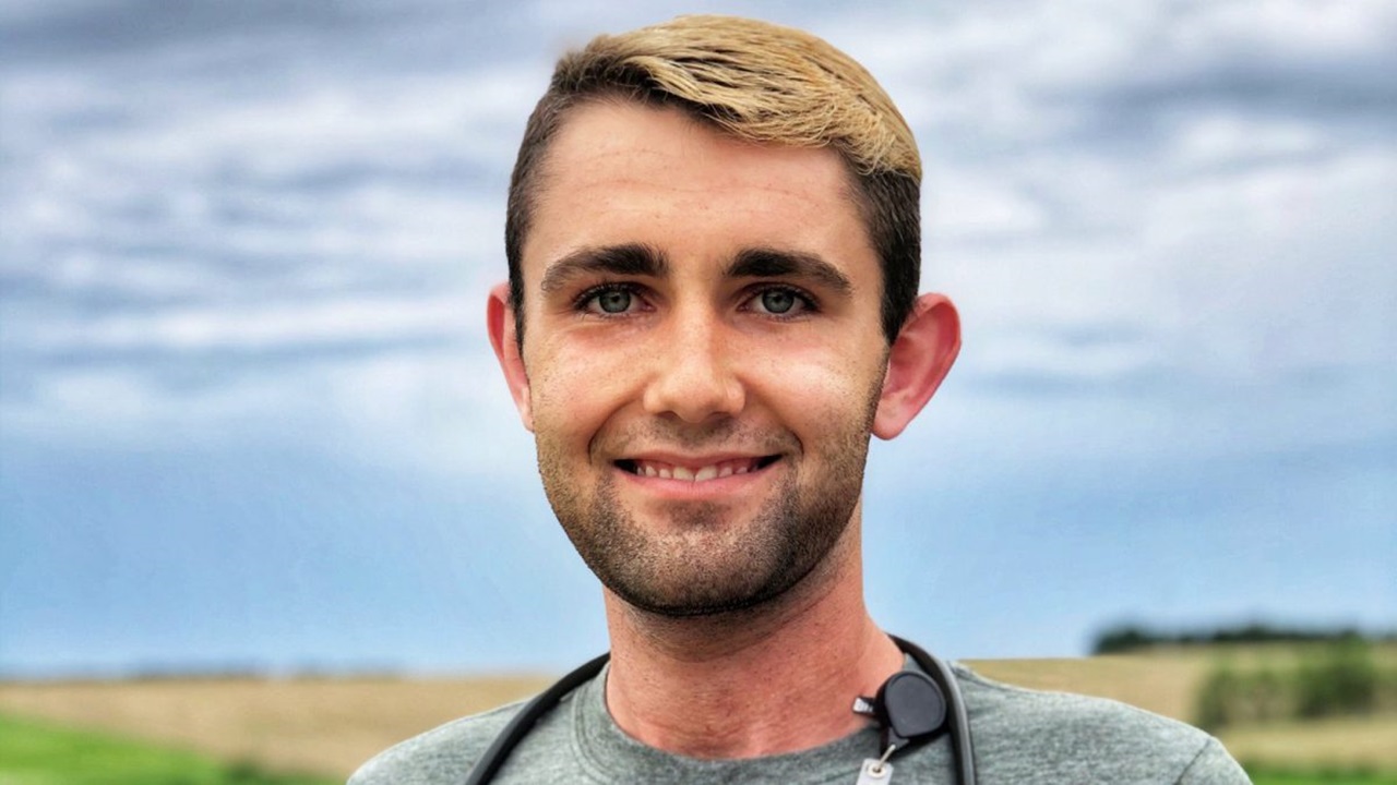 Nathan Popp smiles for a photo in a field with a blue sky behind him.