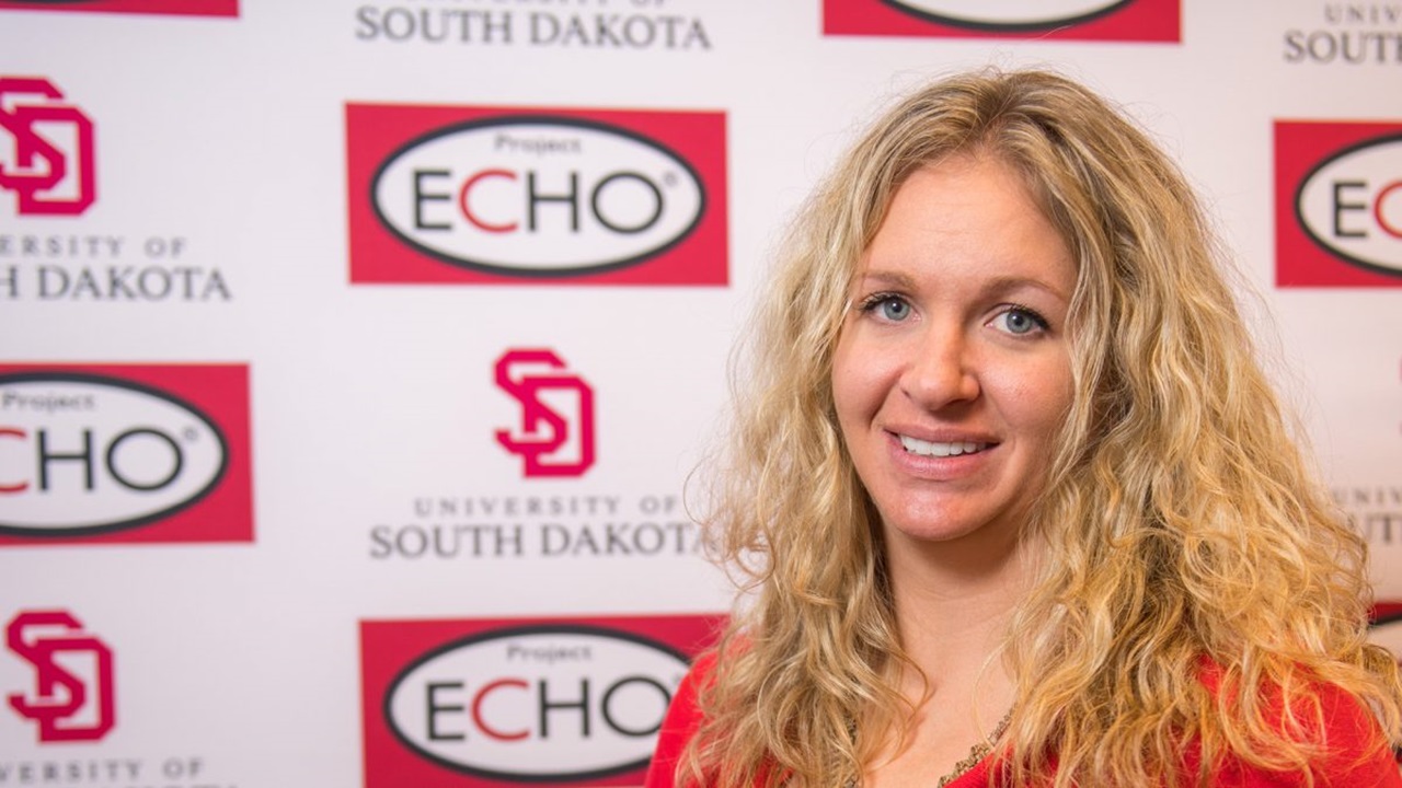 A woman smiles in front of a white USD and ECHO banner.
