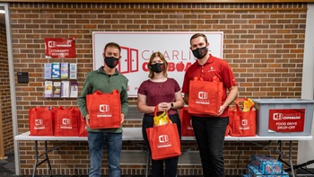 Three people hold red bags and smile at Charlie's Cupboard on USD's campus.