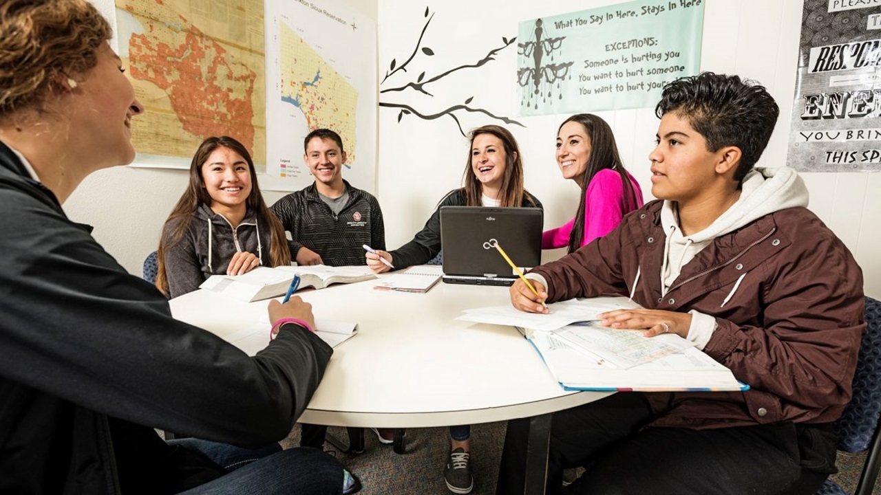 A group of people sits around a table. They are taking notes and smiling.