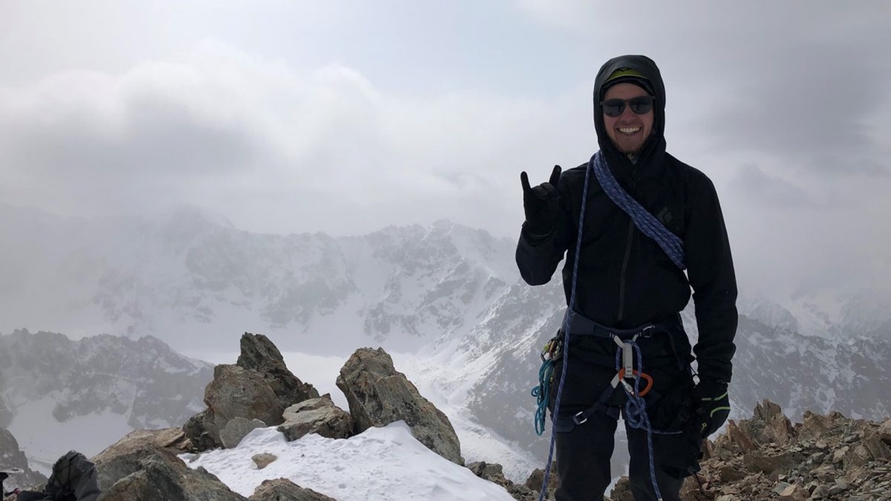 Ross Oyler smiles at the top of a mountain. There is snow and fog in the background.