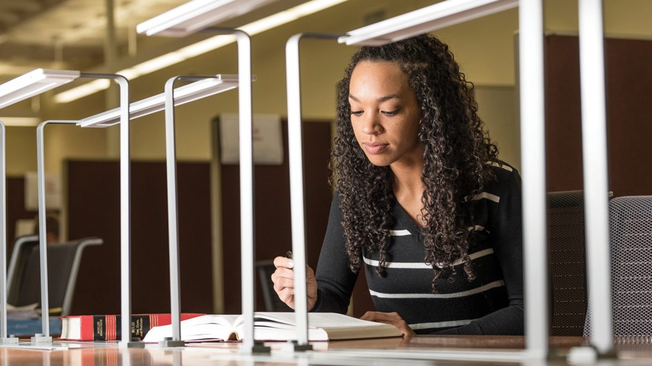 A girl looks down at a book on a table and takes notes.