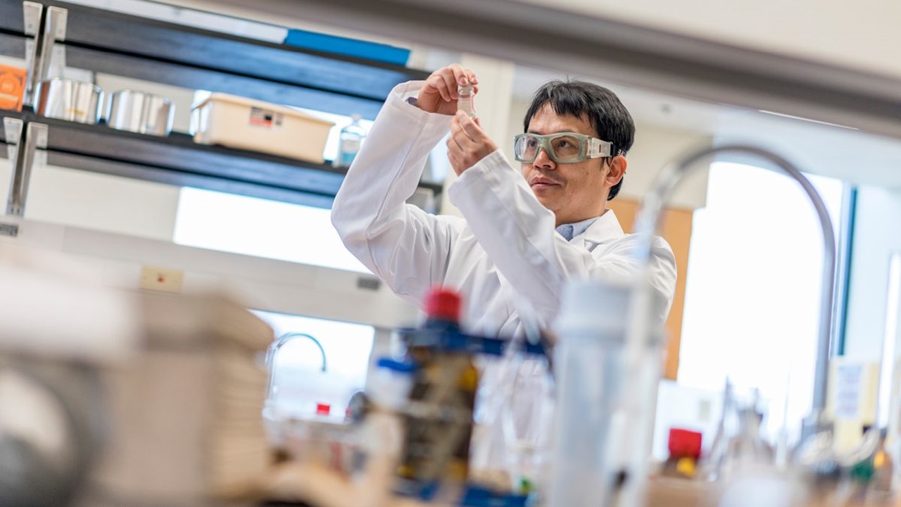 A man holds up a little glass jar in a lab and examines the liquid inside it.