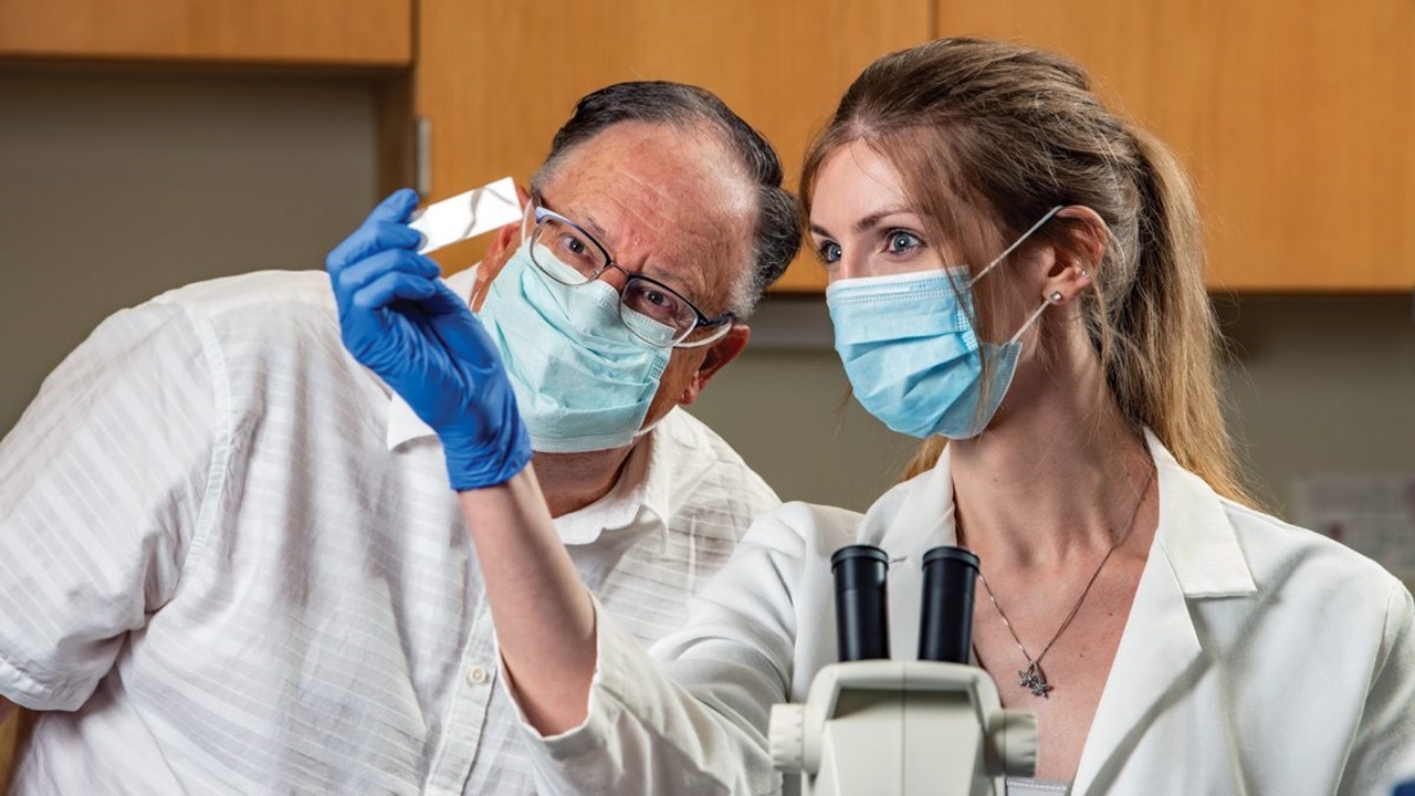 A student and a professor look at a microscope slide in a lab.