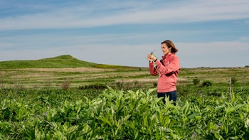 Meghann Jarchow stands in a field of green plants. She is observing one of them in her hand.