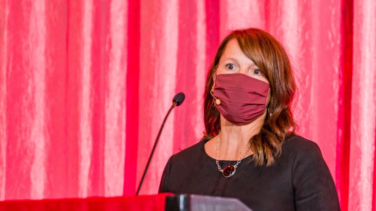 Woman stands at a podium in front of a red screen.
