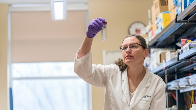 Lisa McFadden examines a test tube with a clear liquid inside.