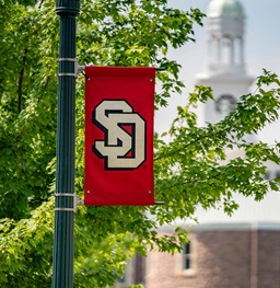 A USD Flag in front of old main.