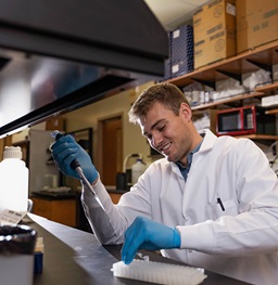 A research student smiling while using a dropper in a lab.
