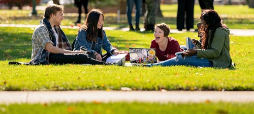 A group of students laying on the campus lawn and laughing.