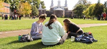 Three students sitting on the MUC lawn doing homework in front of old main.
