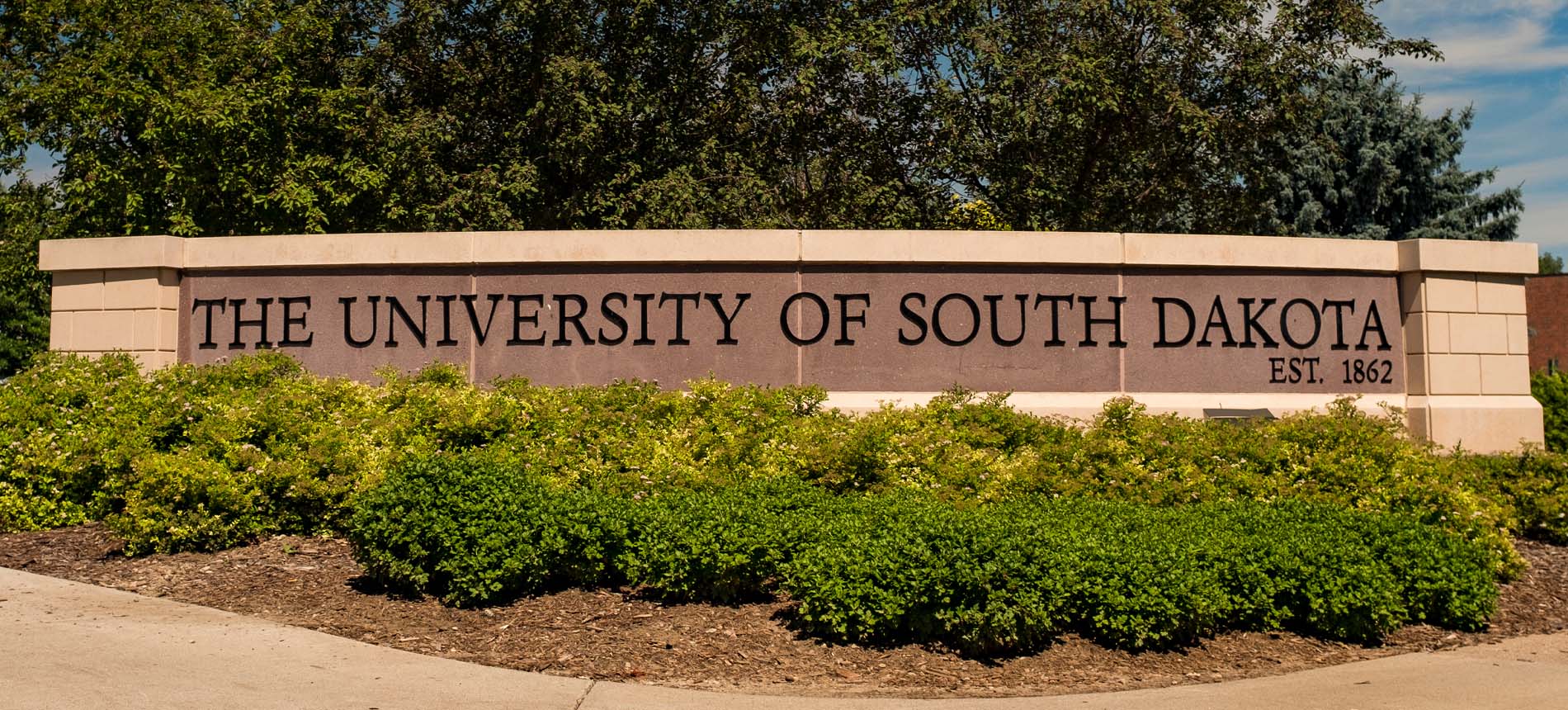 University of South Dakota Sign Behind Shrubs