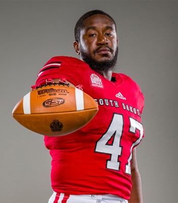 Success story DeValon Whitcomb holding a football in his USD uniform.