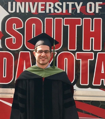 Success story Nicklaus Arra smiling in a cap and gown at USD.