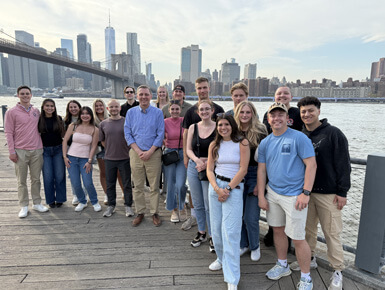 USD students stand in a group, smiling at the camera, with the NYC skyline in the background during the day.